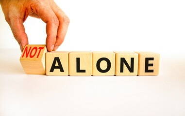 You are not alone symbol. Businessman turns wooden cubes and changes concept words alone to not...