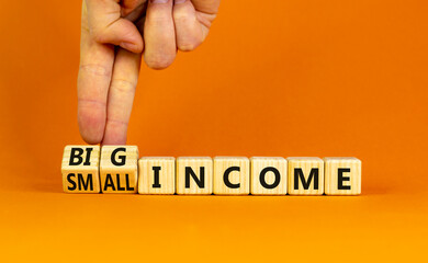 Big or small income symbol. Businessman turns wooden cubes and changes words Small income to Big income. Beautiful orange table orange background, copy space. Business big or small income concept.