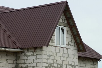 attic of a white brick house with one window under a brown tiled roof against a gray sky