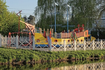 playground with a model of a large colored ship behind a white wooden fence in green grass on the...