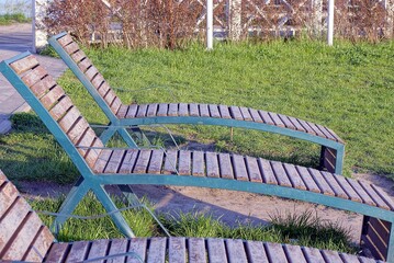 a row of brown wooden benches sunbeds stand in the green grass in the park on the street