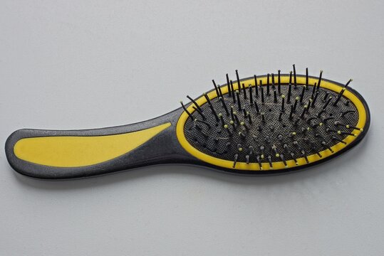 One Large Plastic Black Yellow Dirty Hairbrush Lies On A White Table