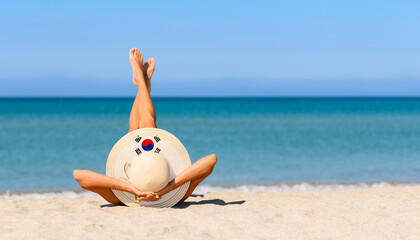 A slender girl on the beach in a straw hat in the colors of the South Korea flag. The concept of a perfect vacation in a resort in the South Korea. Focus on the hat.