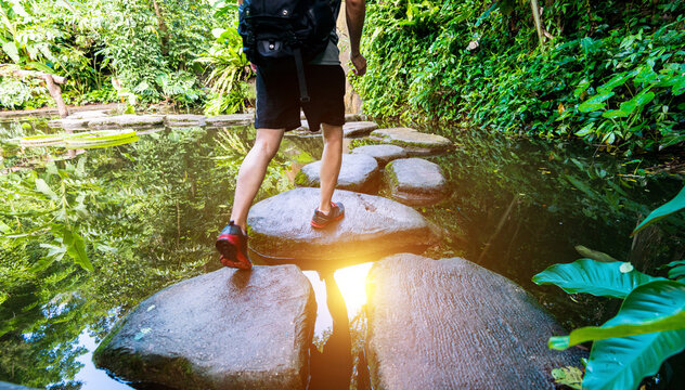 Male hiker with backpack crossing a river on stones