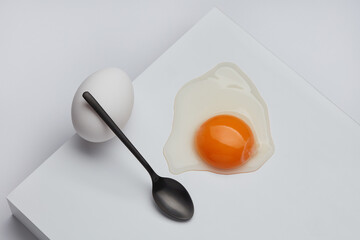 Still life of white whole egg and broken egg with a yolk with black spoon on a white background. Shallow depth of field