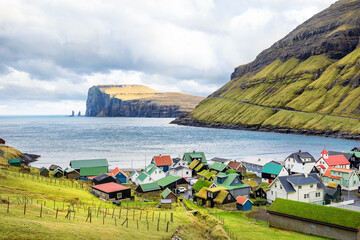 Seaside Tjornuvik  village in Eysturoy in Faroe Islands surrounded by grassy hills and rugged cliffs on a cloudy day with North Atlantic Ocean views.  Panoramic view