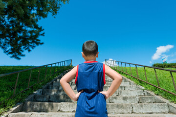 Rear view of little boy standing by steps outdoors with his hands on hips