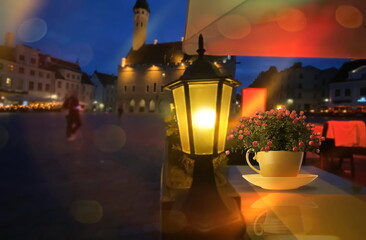 cup with flowers   on restaurant  table evening old vintage lanter light   on medieval street pavement and houses in Tallinn old town hall square  Estonia