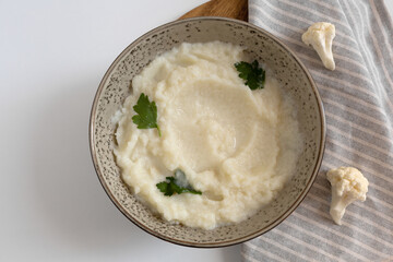 mashed cauliflower puree in bowl with herbs and raw cauliflower. paleo diet. top view