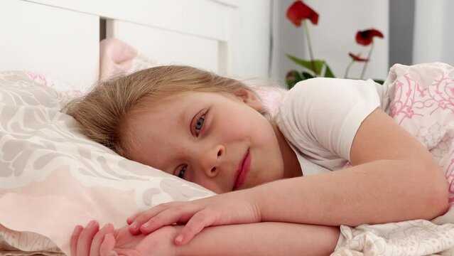child sleeping. A little beautiful girl with blue eyes woke up in bed. The child lies in bed and smiles. Wide open baby blue eyes. Happy childhood. Children's sleep, rest.