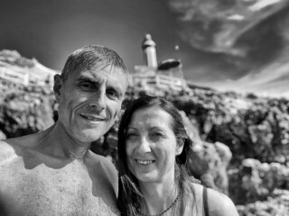 Grayscale selfie of an Italian couple on a beach with a blurred background