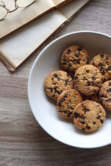 Plate of chocolate chip cookies, open books and reading glasses on wooden table. Flat lay.