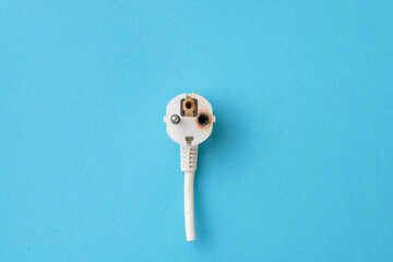 Old electric plug with traces of fire due to a short electrical circuit, blue background, flat lay,...