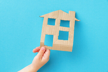 The child cuts a cardboard house in his hands on a blue background, close-up.