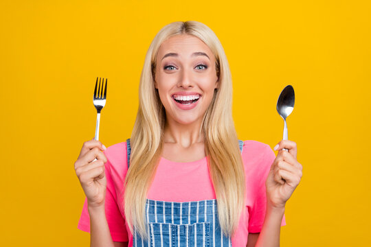 Portrait of attractive cheerful amazed girl holding in hands cutlery waiting meal isolated over bright yellow color background