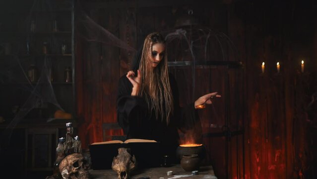Halloween, witch use magic book and cauldron prepare poison or love potion. Black magic occult female wizard in dark room cage spider web human skull Necromancer cooking magic potion. voodoo. Handheld