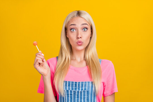 Portrait of attractive funny girly teenage girl licking candy staring eyes pout lips isolated over bright yellow color background
