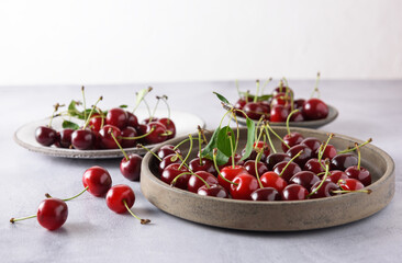 Fresh organic cherries in a grey ceramic plate. Behind there are white and gray plates with cherries. Close-up, copy space.