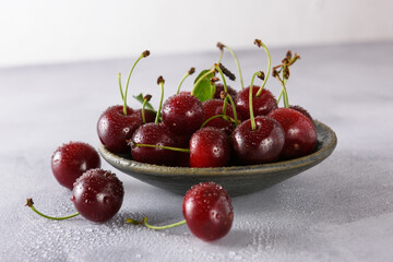 Fresh red cherry in drops of water in a gray ceramic saucer on a light background. Close-up.