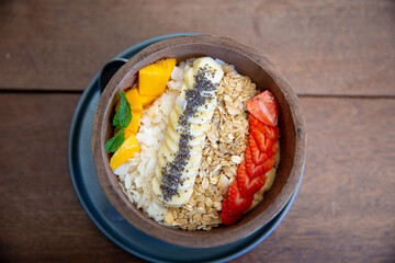 Mango smoothies bowl with berries, granola, chia seeds and coconut on wooden background