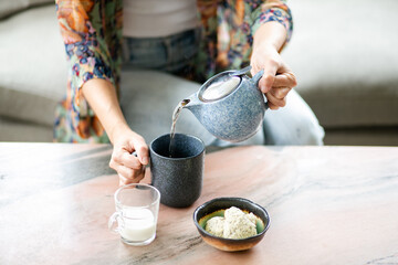 cropped photo of woman sitting at coffee table pouring herself tea