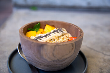 Mango smoothies bowl with berries, granola, chia seeds and coconut on concrete background