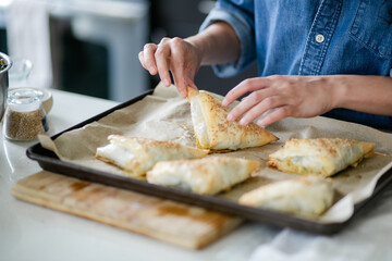 Cropped photo of woman taking homemade spanakopita off baking sheet
