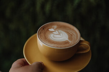 cropped shot of Woman holding cup of hot cappuccino on green background, top view.
