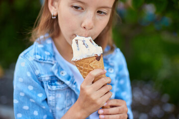 Cute girl liccking and eating italian ice cream cone while resting in park on summer day
