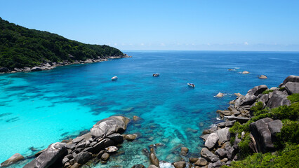 Fototapeta premium Turquoise water in the bay. View of the island and the sea. High cliffs covered with green trees. The gradient of water from blue to blue. There are speedboats, people swim in places. Similan Islands