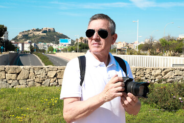 A 60 year old man wearing sunglasses, on summer vacation sightseeing in the city of Alicante,...