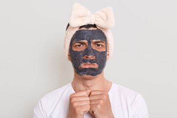 Portrait of sad offended handsome man with mud dirt cosmetology mask, doing cosmetic procedures at...