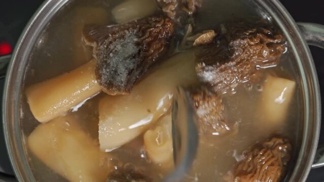 The cook cooks morel mushrooms and adds salt to the water boiling in a saucepan