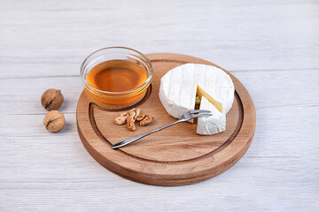 Fresh brie cheese and a slice on a round wooden board, walnut and honey, on a light background, space for text