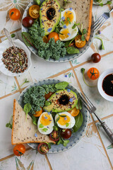 Healthy lunch with avocado halves, cherry tomatoes, soft-boiled eggs, kale, wheat bread, seeds and soy sauce flavored with edible flowers.