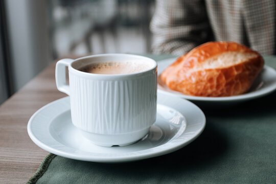 A cup of coffee and a bun on the breakfast table in a cafe