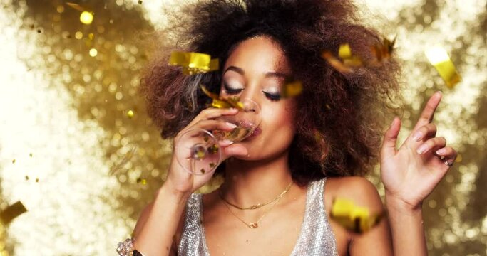 Young african american woman with an afro celebrating at a party drinking a glass of champagne and dancing. Carefree young woman dancing and drinking champagne while gold confetti falls
