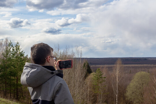 A teenage boy takes pictures on a smartphone of the landscape of a swamp in spring or autumn