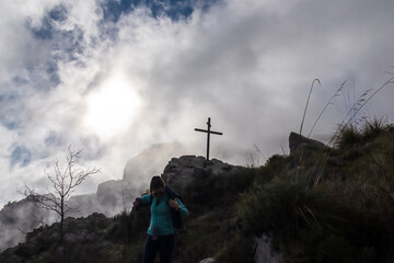 Silhouette of woman hiking through clouds from summit cross near Santa Maria del Castello. Scenic...