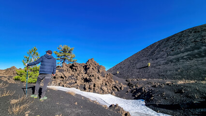 Tourist man with hiking pole and camera at crater of Sartorio on volcanic landscape of volcano...