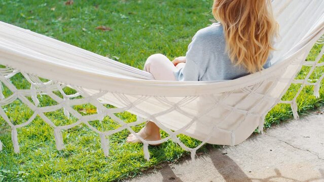 Young woman relaxes in the hammock in the garden with green grass