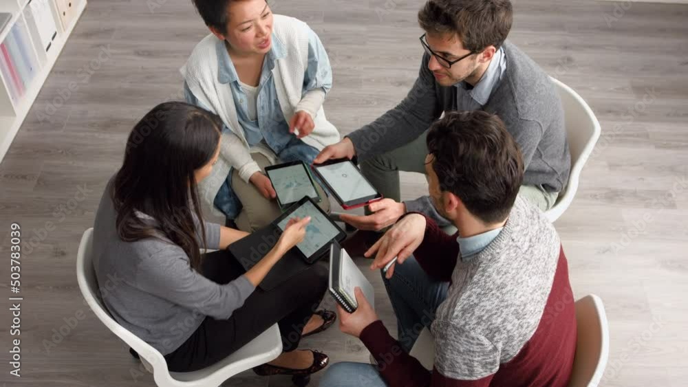 Aufkleber Diverse group of happy young businesspeople using digital tablets during a brainstorming meeting. A group of business colleagues using tech tablets to talk and collaborate during planning sessions.