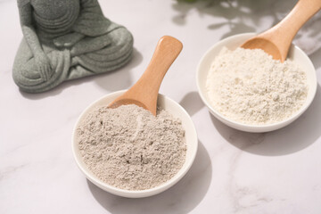 White bowls with gray and white cosmetic clay on white marble table - mineral powder, bentonite facial mask. Skincare beauty concept. Selective focus