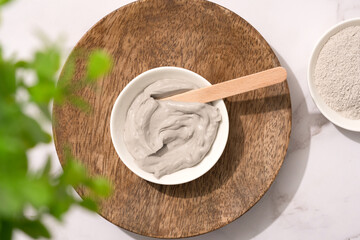 Bowl with gray cosmetic clay cream on wooden tray - mineral bentonite facial mask. Skincare beauty concept. Top view - obrazy, fototapety, plakaty