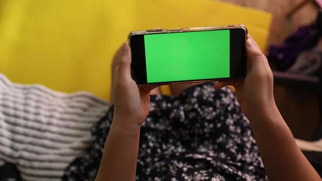Woman at Home sitting on a Couch using Smartphone with Green Mock-up Screen, Doing Swiping, Scrolling Gestures. Girl Using Mobile Phone, Internet Social Networks Browsing.