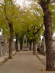 Shrine with statue of a kneeling women in a lane with grave chapels and trees in Alto de Sao Joao cemetery, Lisbon, Portugal 