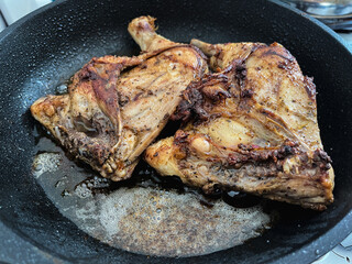 Two chicken legs are fried in a pan in a large amount of oil.