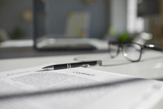 Some paper documents ready for signing on table. Employment or insurance contract agreement, pen, and glasses placed on office desk. Close up. Soft, selective focus