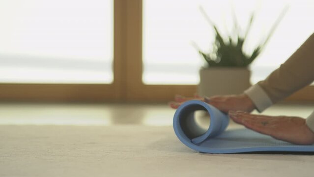 CLOSE UP. Unrecognizable person unrolling blue yoga mat, preparing for workout at home. Female hands unfolding exercise mat for indoor leisure activity. Getting ready for meditation and relaxation.