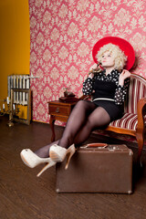 Curly girl - blonde in a blouse with polka dots - pin-up, with a suitcase calls on an old telephone in a red room
